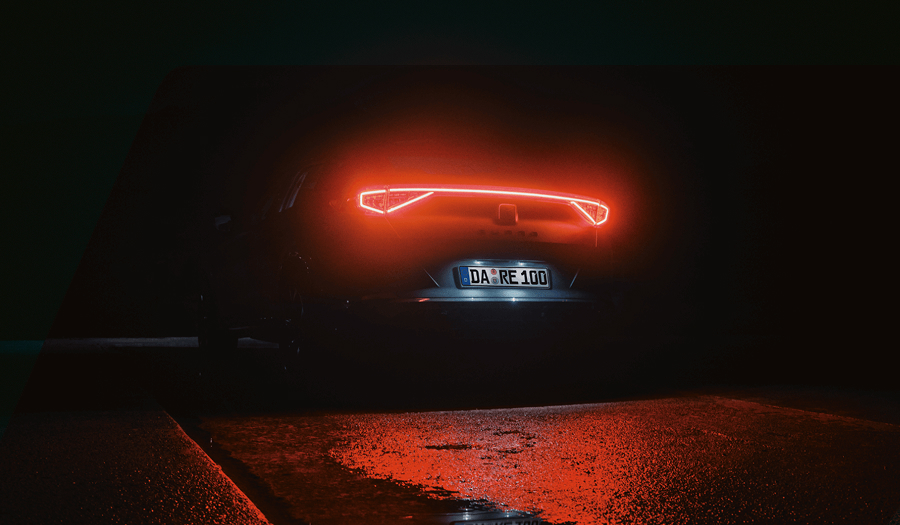 Rückansicht eines CUPRA Fahrzeugs bei Nacht mit leuchtendem durchgehendem Rücklicht.